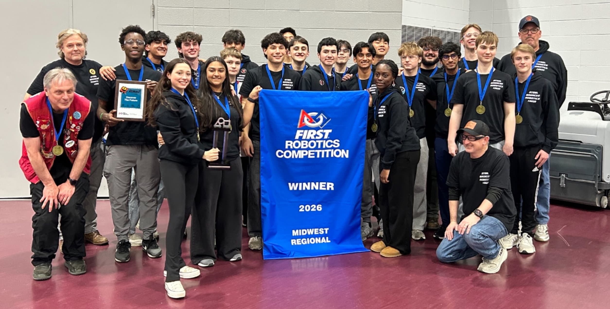 Team 8029 with the FIRST Robotics Competition winner banner for the 2026 Midwest Regional, wearing medals and holding the trophy