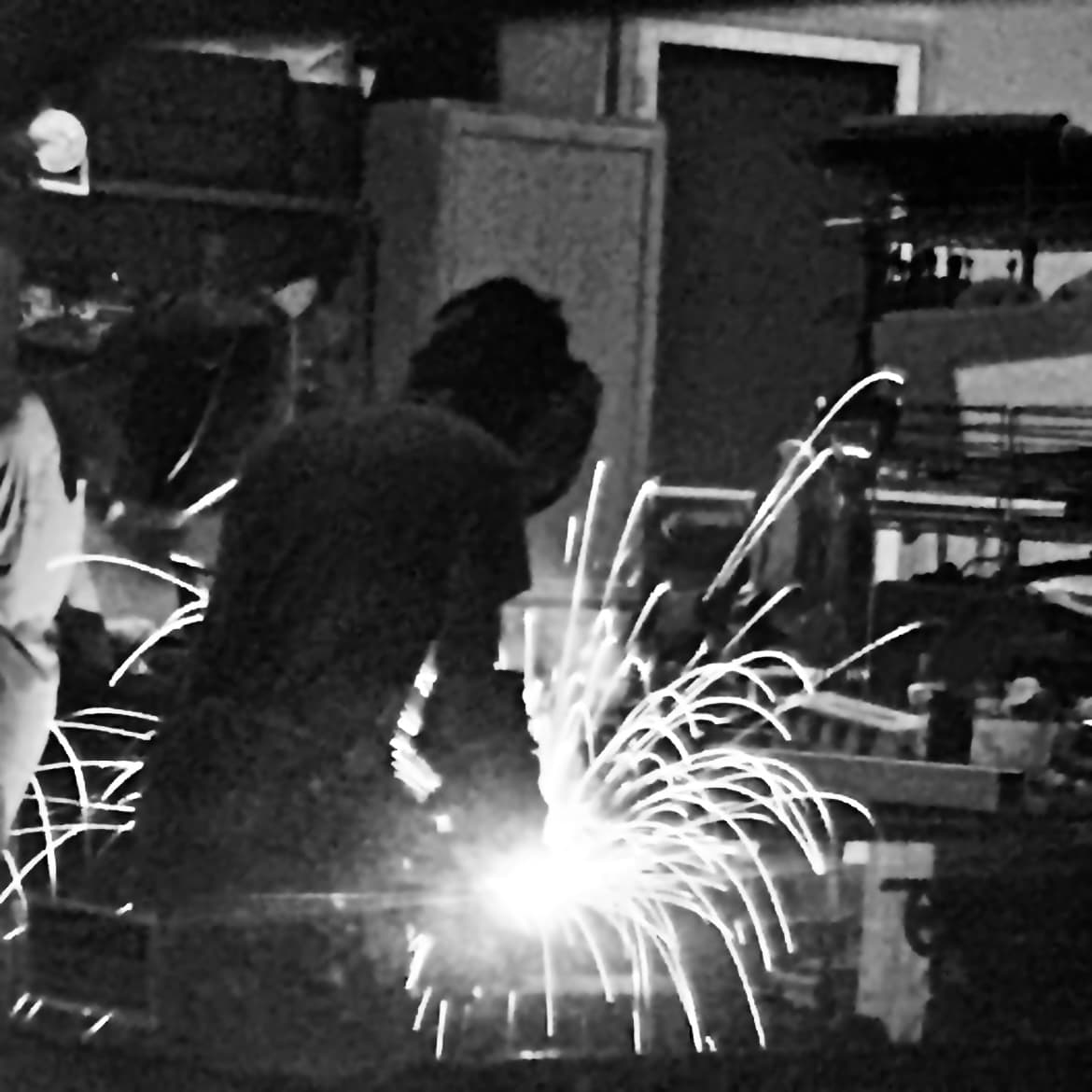 A student welding a part in the shop, sparks arcing out across the bench